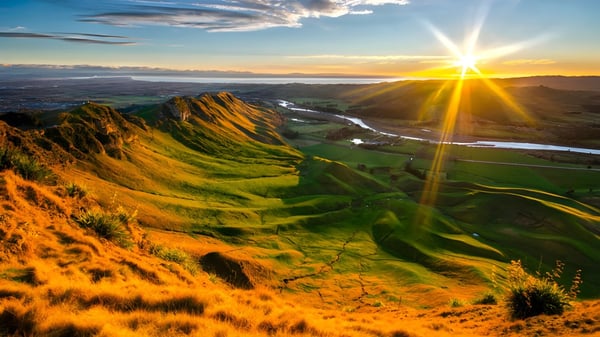 Sanft hügelige, grüne Landschaft bei Sonnenuntergang mit einer entfernten Stadt im Hintergrund nahe Woodford House.