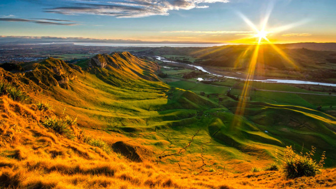 Grüne Hügel mit Vegetation und einer fernen Stadt sind bei Sonnenuntergang zu sehen, nahe Woodford House.