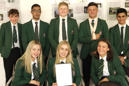 Eine Gruppe von Schülern der Woodhouse Grove School in grüner Schuluniform posiert in einem Schulgebäude vor Bildern an der Wand.