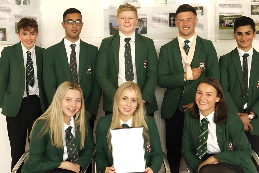 Eine Gruppe von Schülern der Woodhouse Grove School in grüner Schuluniform posiert in einem Schulgebäude vor Bildern an der Wand.