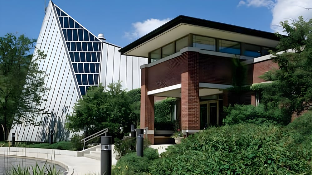 Das moderne mehrstöckige Gebäude mit Glasfassade der Woodlands Academy of the Sacred Heart ist von Bäumen und gepflegter Landschaft umgeben.