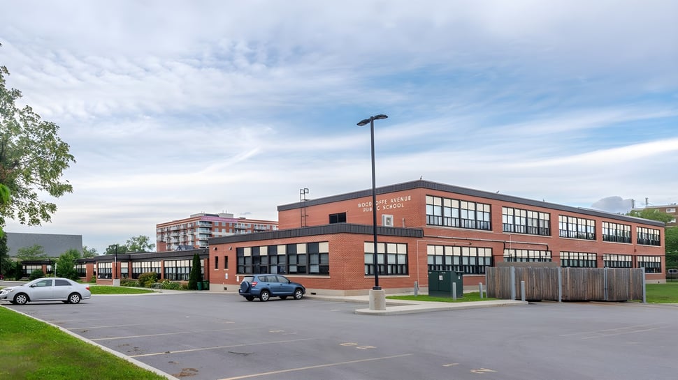 Das mehrstöckige Backsteingebäude der Woodroffe High School mit großen Fenstern und davorliegendem Parkplatz präsentiert sich bei bewölktem Himmel.