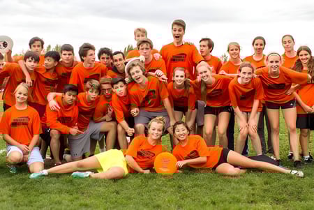 Eine Gruppe von Schülerinnen und Schülern der Woodroffe High School steht auf einem Grasfeld und trägt orange Shirts.
