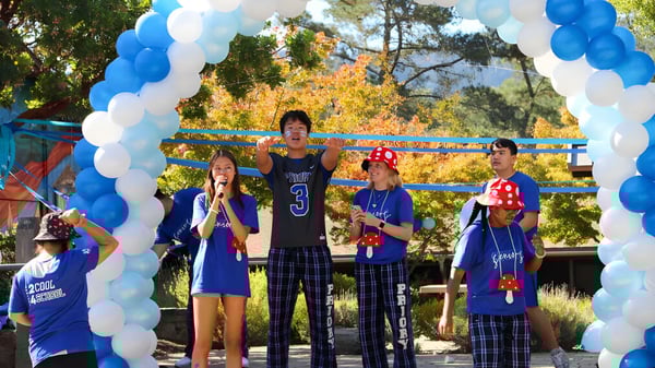 Eine Gruppe Schülerinnen und Schüler der Woodside Priory School steht vor einem Luftballonbogen im Freien mit Bäumen im Hintergrund.