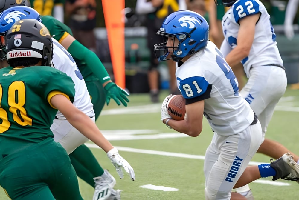 Zwei Football-Spieler gegenüberstehen sich auf dem Spielfeld der Woodside Priory School mit weiteren Spielern im Hintergrund.