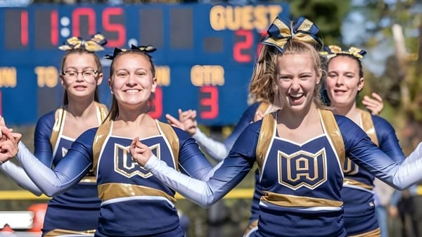 Schülerinnen der Woodstock Academy in einheitlichen Cheerleader-Uniformen stehen vor einer Anzeigetafel mit Spielstand.