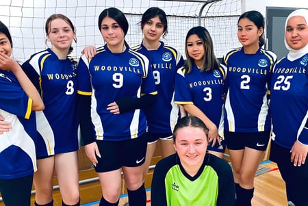 Eine Gruppe junger Volleyballspielerinnen der Woodville High School posiert gemeinsam auf dem Volleyballfeld.