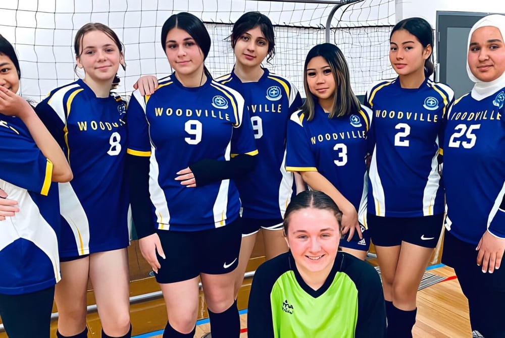 Eine Gruppe junger Volleyballspielerinnen der Woodville High School posiert gemeinsam auf dem Volleyballfeld.