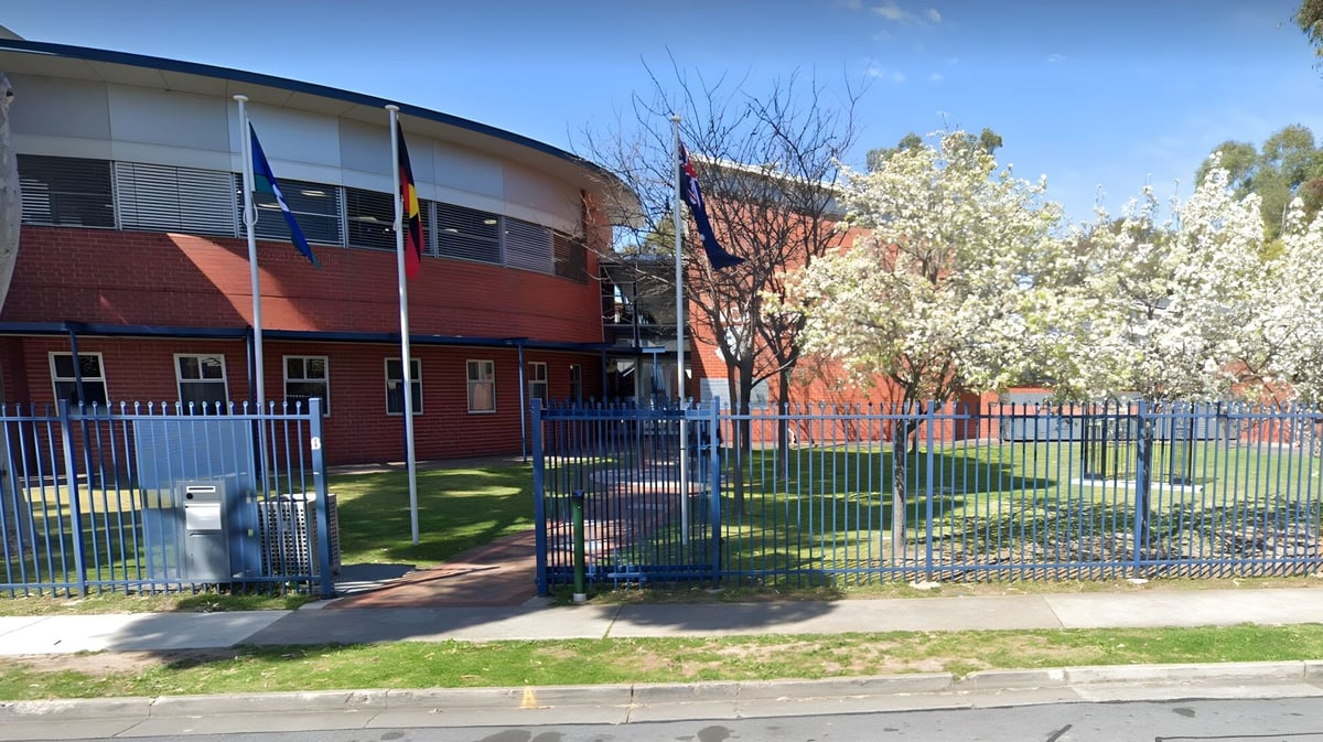 Das moderne mehrstöckige Hauptgebäude der Woodville High School mit gewölbtem Dach steht vor eingezäuntem Grün und blühenden Bäumen.