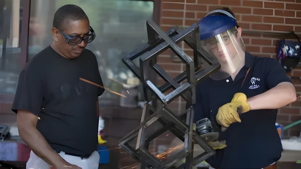 Zwei Personen arbeiten an einem Metallrahmen vor einer Backsteinwand auf dem Gelände der Woodward Academy.