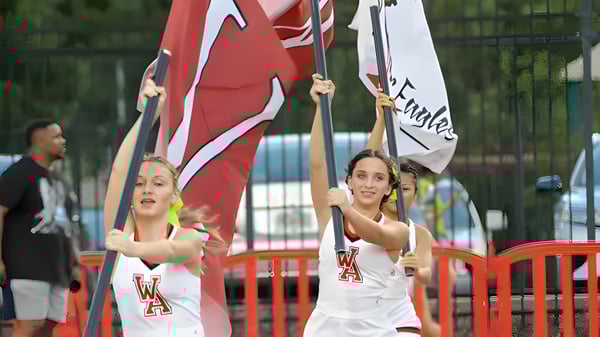 Schüler der Woodward Academy halten Fahnen und Banner bei einer öffentlichen Demonstration vor einem umzäunten Bereich.