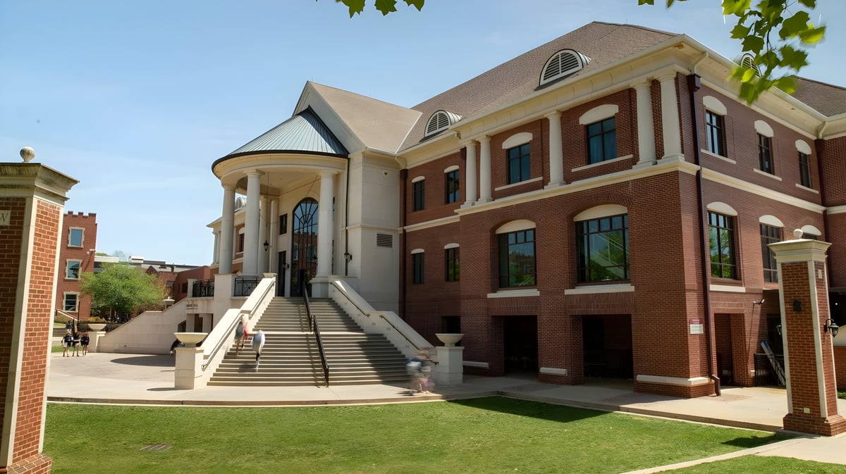 Das Backsteingebäude der Woodward Academy mit Säuleneingang und großen Fenstern steht auf einer Rasenfläche mit Bäumen.