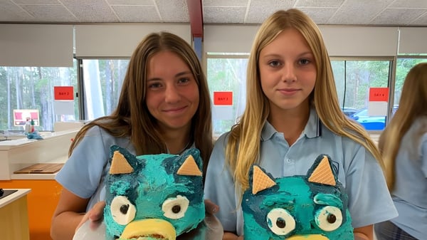 Zwei Schülerinnen der Woolgoolga High School tragen einheitliche Shirts mit Monster-Design und stehen in einem Klassenraum.