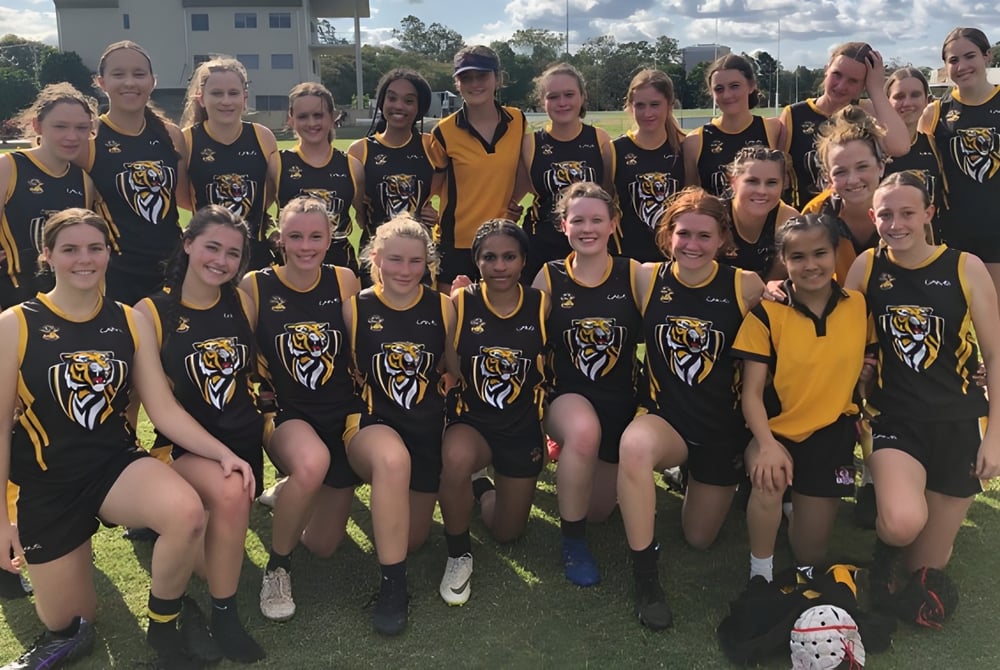 Eine Gruppe junger Athletinnen posiert im Sportdress auf einer Wiese vor einem Gebäude auf dem Campus des Worksop College.