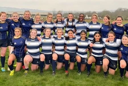 Eine Gruppe junger Fußballspielerinnen posiert in einheitlichen Trikots auf dem Sportplatz der Worth School vor einem Wald.