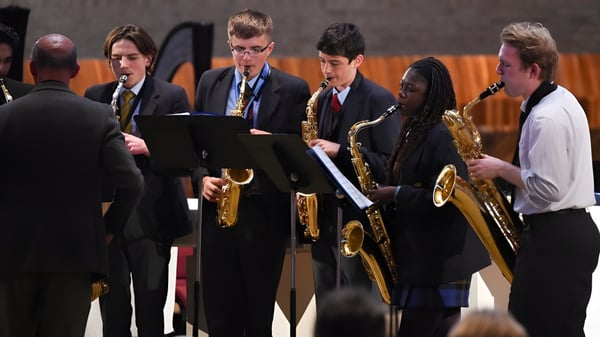 Schüler der Worth School stehen in formeller Kleidung auf einer Bühne und bereiten sich mit Musikinstrumenten auf einen Auftritt vor.