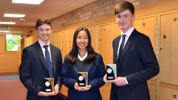 Drei Schüler der Worth School stehen im Schulflur vor Schließfächern und halten Auszeichnungen in den Händen.