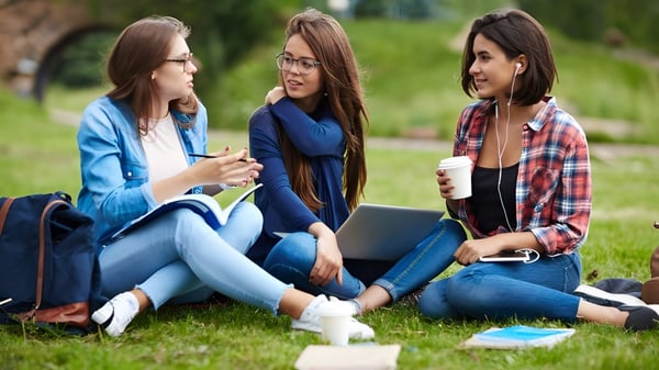 Drei Schülerinnen der Worthgate School Canterbury sitzen auf der Wiese und unterhalten sich vor grünem Hintergrund.