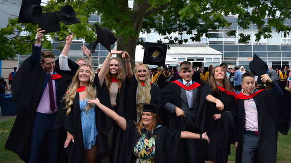 Eine Gruppe Absolventen in Talaren versammelt sich vor einem Gebäude auf dem Campus des Worthing College.