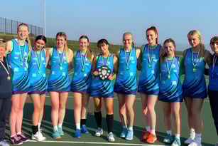 Eine Gruppe junger Athletinnen in blauen und weißen Sportuniformen mit Medaillen steht auf dem Sportplatz des Worthing College.