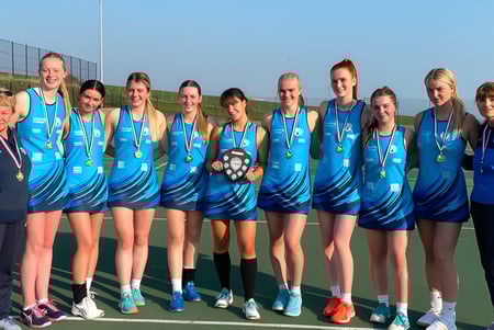 Eine Gruppe junger Athletinnen in blauen und weißen Sportuniformen mit Medaillen steht auf dem Sportplatz des Worthing College.