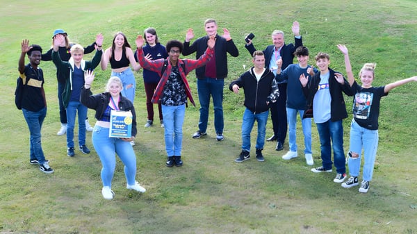 Schüler und Erwachsene stehen gemeinsam auf einer Wiese auf dem Gelände des Worthing College und winken mit den Armen.