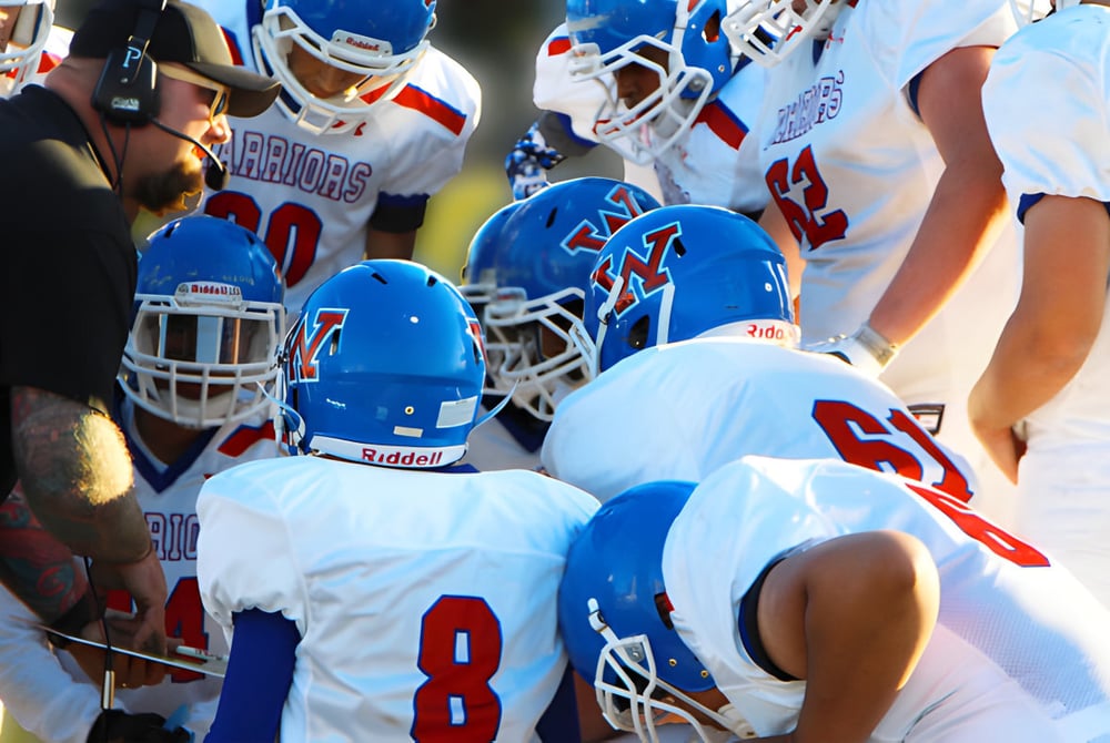 Eine Gruppe von Footballspielern in weißen und blauen Uniformen spielt auf dem Feld der W.P. Wagner High School.