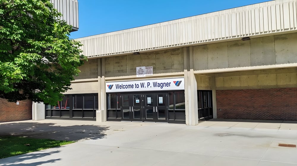 Das Gebäude der W.P. Wagner High School mit einem Willkommensschild über dem Eingang ist von Bäumen und Grünflächen umgeben.