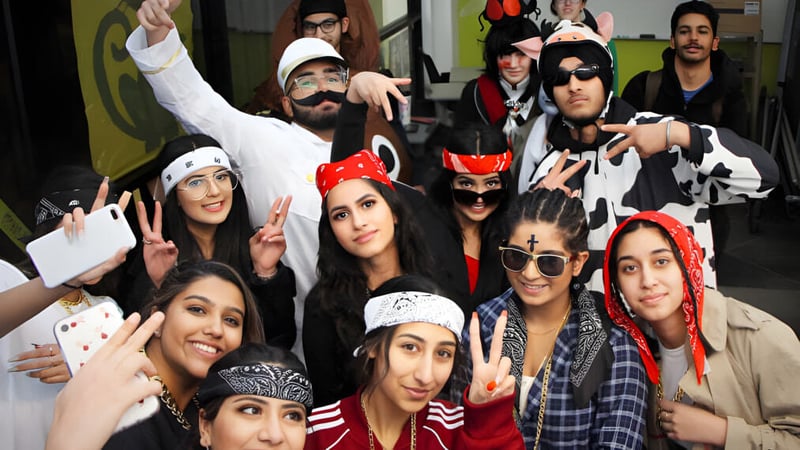 Eine Gruppe von Schülerinnen und Schülern der W.P. Wagner High School posiert in verschiedenen Kostümen vor einem farbenfrohen Hintergrund.