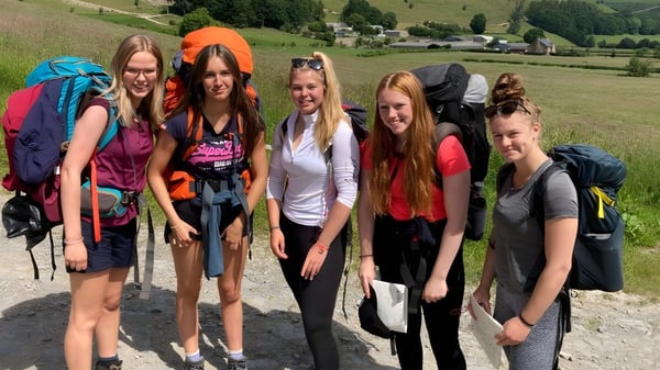 Eine Gruppe Schülerinnen von Wrekin College steht gemeinsam in Wanderkleidung vor einer hügeligen Landschaft.
