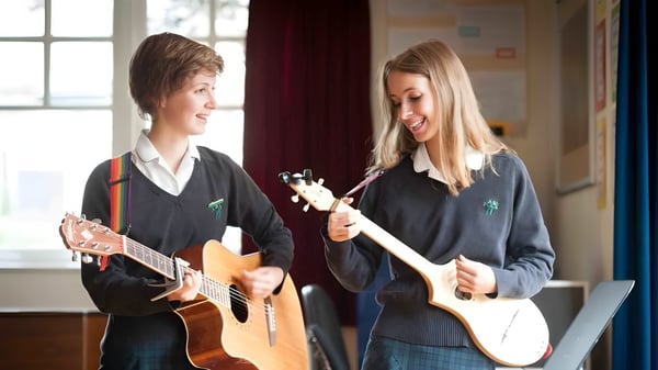 Zwei Schülerinnen der Wychwood School spielen gemeinsam akustische Gitarren in einem Klassenraum mit Fenster im Hintergrund.