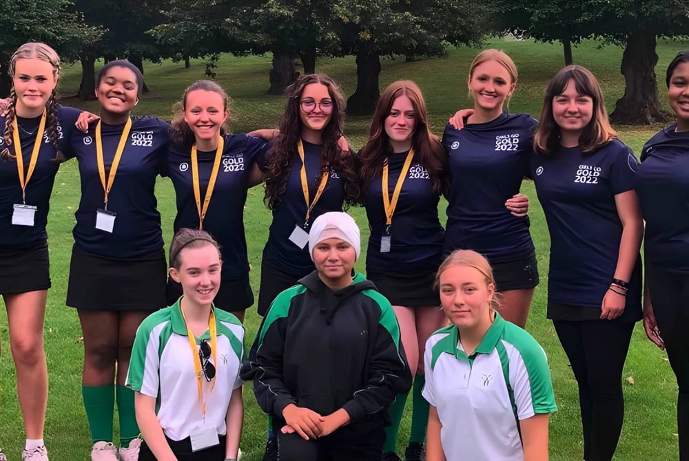 Eine Gruppe junger Schülerinnen der Wychwood School steht in Sportuniformen auf einer Wiese im Freien.