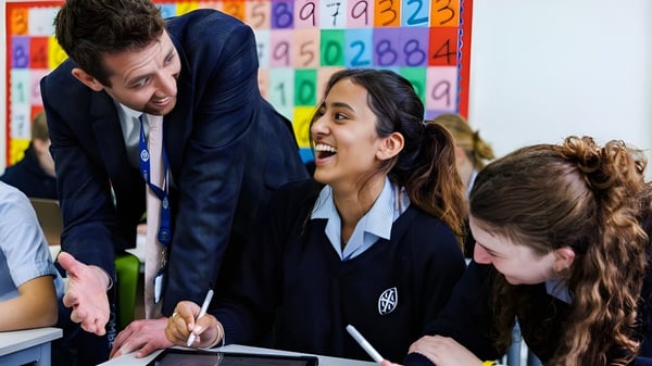 Eine Gruppe Schüler der Wycombe Abbey School diskutiert mit ihrer Lehrerin im Klassenzimmer vor bunten Lernplakaten.