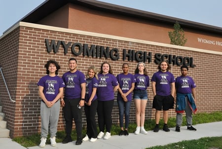 Eine Gruppe Schüler steht vor dem Gebäude der Wyoming High School mit dem Schulnamen an der Fassade.