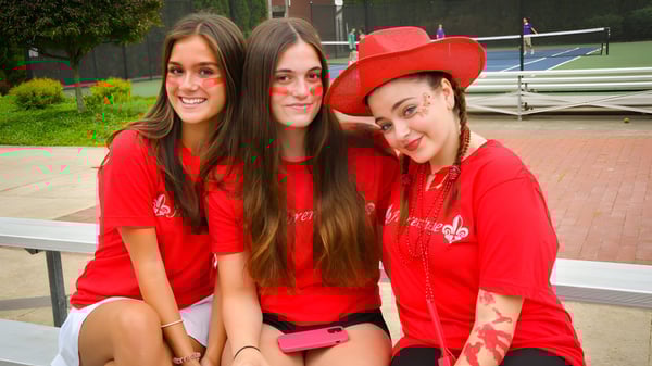 Drei Studentinnen der Wyoming Seminary College Preparatory posieren lächelnd zusammen im Außenbereich vor einem Gebäude mit Grünpflanzen.