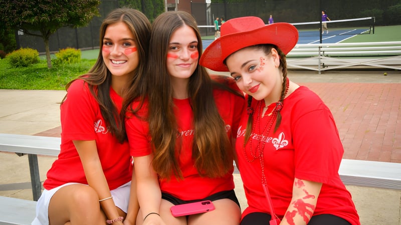 Drei Studentinnen der Wyoming Seminary College Preparatory posieren lächelnd zusammen im Außenbereich vor einem Gebäude mit Grünpflanzen.
