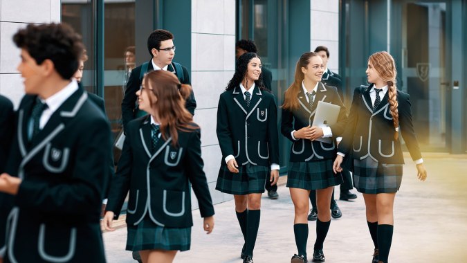 Eine Gruppe Schüler in Uniformen geht gemeinsam im Flur der Yago School mit Glaswänden und Türen.
