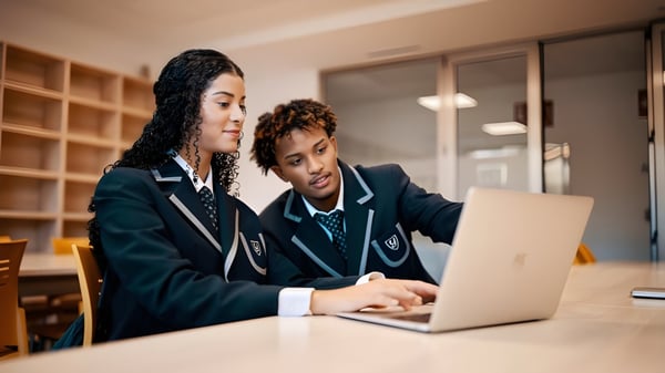 Zwei Schüler der Yago School arbeiten konzentriert an einem Laptop in einem Bereich mit Bücherregalen.