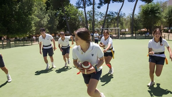 Eine Gruppe Schüler in Sportuniformen steht auf dem Sportfeld der Yago School mit Bäumen und Gebäuden im Hintergrund.