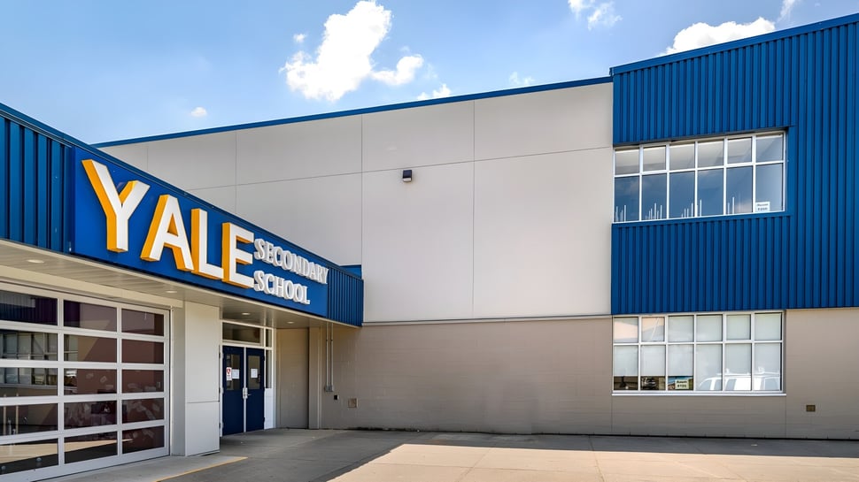 Das große blau-weiße Industriegelände der Yale Secondary School vor einem wolkigen Himmel.