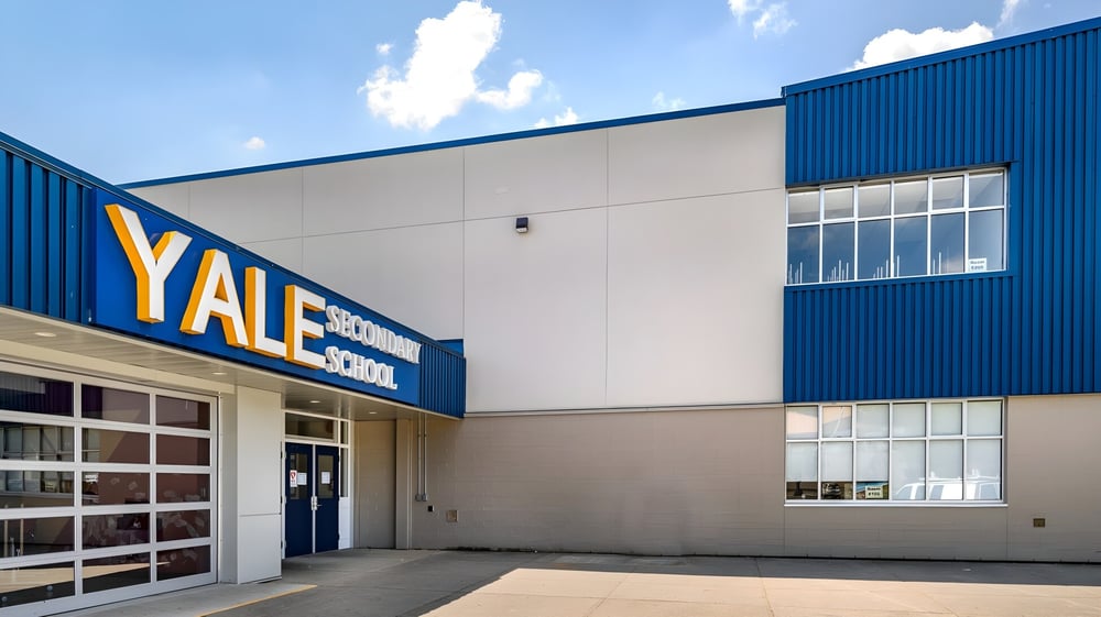 Das große blau-weiße Industriegelände der Yale Secondary School vor einem wolkigen Himmel.