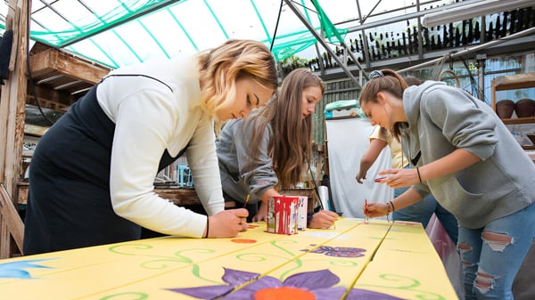 Eine Gruppe von Schülerinnen und Schülern der Yale Secondary School sitzt gemeinsam an einem Tisch und arbeitet an einer Aufgabe vor einem bunten Wandbild.