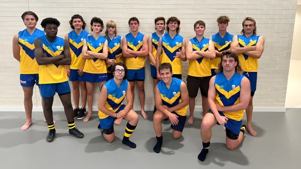 Eine Gruppe von Schülerinnen und Schülern des Yanchep Secondary College steht gemeinsam vor einer weißen Wand in blauen und gelben Schuluniformen.