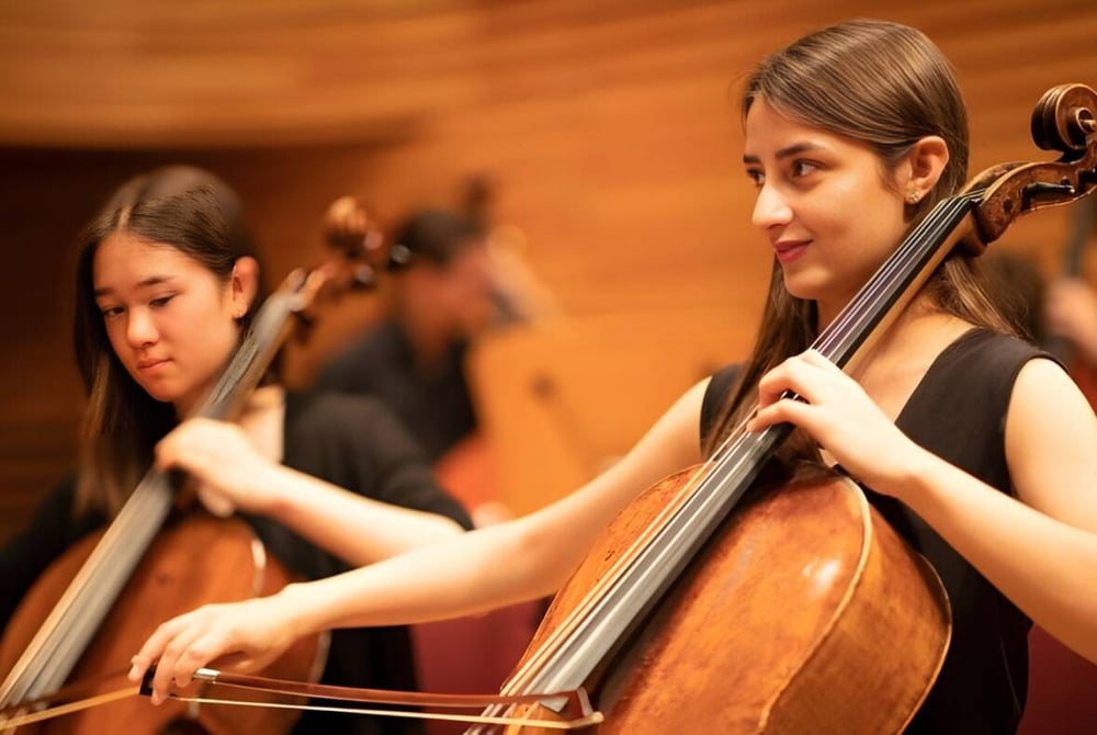 Eine Schülerin der Yehudi Menuhin School spielt Cello auf der Bühne mit einem weiteren Musiker im Hintergrund.