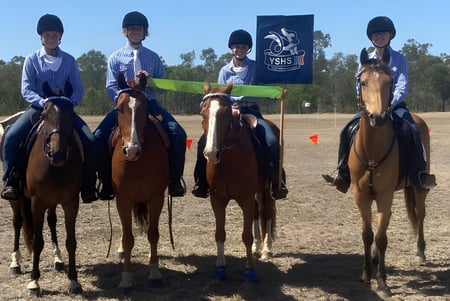 Schüler der Yeppoon State High School reiten in Uniform auf einem Feld mit einer Flagge im Hintergrund.