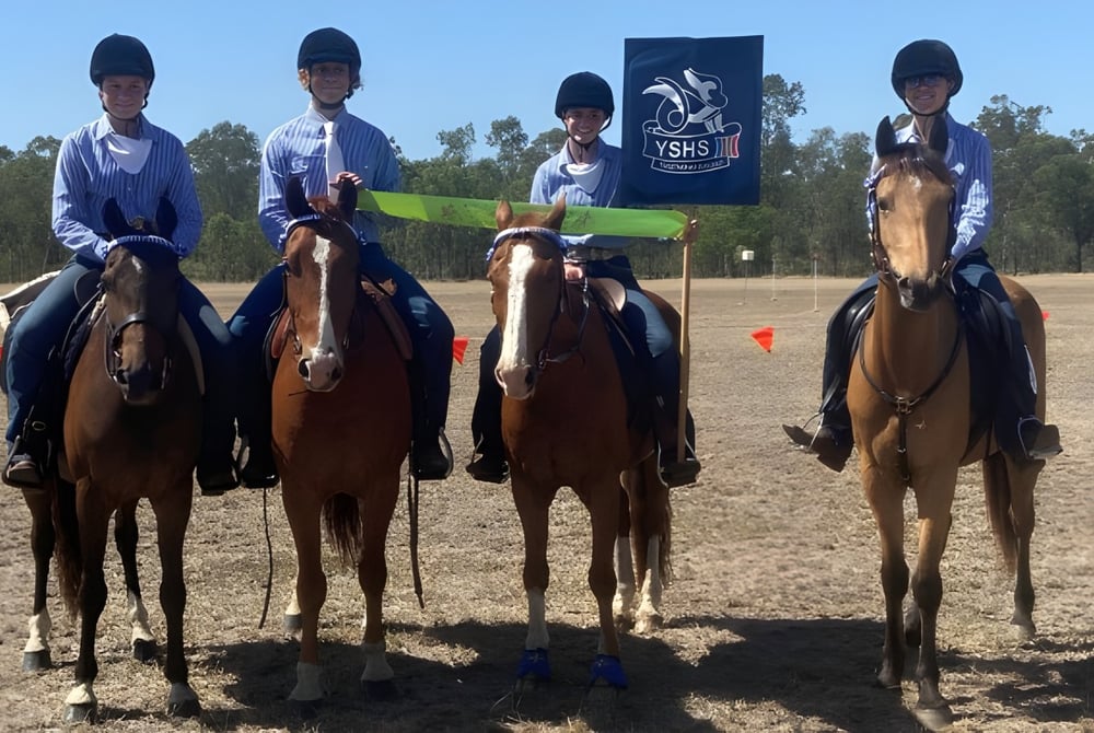 Schüler der Yeppoon State High School reiten in Uniform auf einem Feld mit einer Flagge im Hintergrund.