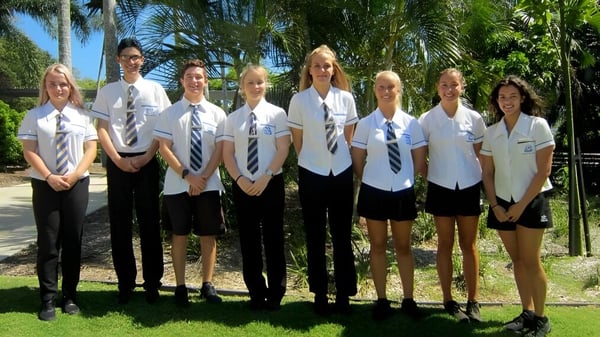 Eine Gruppe Schüler in Schuluniform steht im tropischen Umfeld auf dem Gelände der Yeppoon State High School.