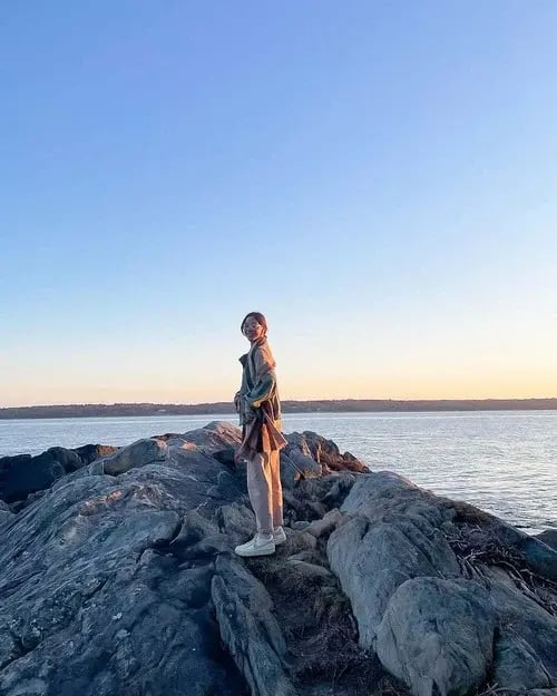 eine Schülerin beim Sonnenuntergang auf einem Felsen vor der Küste