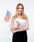 Happy young businesswoman standing with US flag over gray background and looking at camera