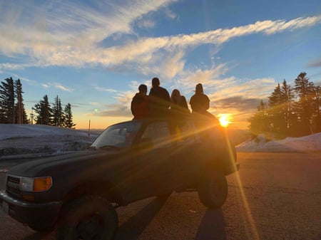 Schwarzes SUV bei Sonnenuntergang mit Schülern auf dem Dach